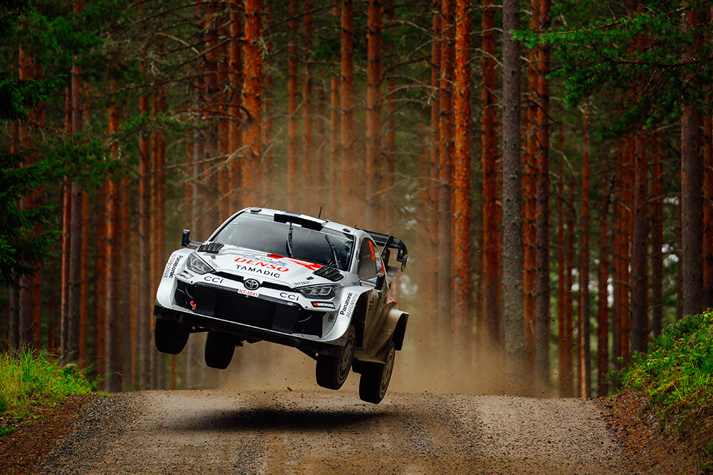 mobil WRC 2025 melompat di gravel Finlandia dengan latar hutan pinus